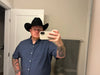 Man wearing a black cowboy hat and blue shirt taking a mirror selfie.