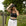 Woman wearing a black cowboy hat, black top, and white skirt in a grassy outdoor setting.