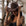 Woman wearing a brown cowboy hat with tattoos on her arms, standing against a blurred natural background.