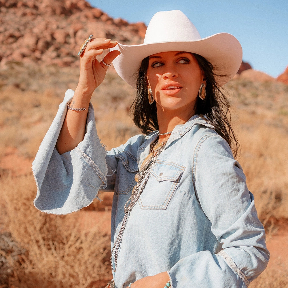 Woman wearing a white hat and denim jacket in a desert setting