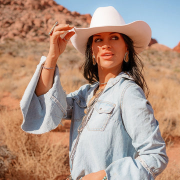 Woman wearing a white hat and denim jacket in a desert setting