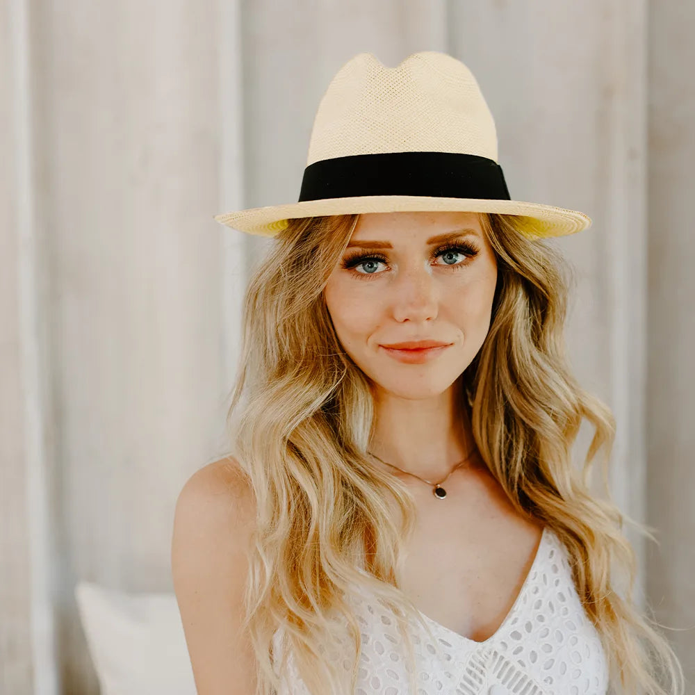 Woman wearing a beige hat with a black band against a neutral background