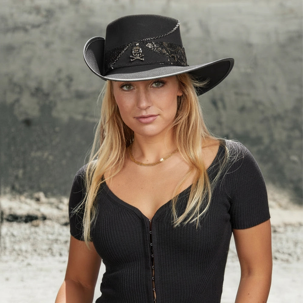 Woman wearing a black cowboy hat with skull design against a textured wall.