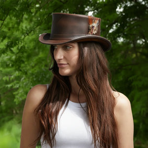 Woman wearing a brown leather hat with a decorative feather against a green leafy background