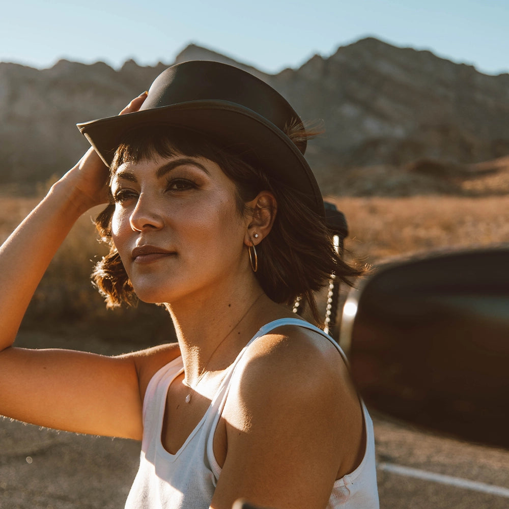 Woman wearing a hat in a desert setting with mountains in the background