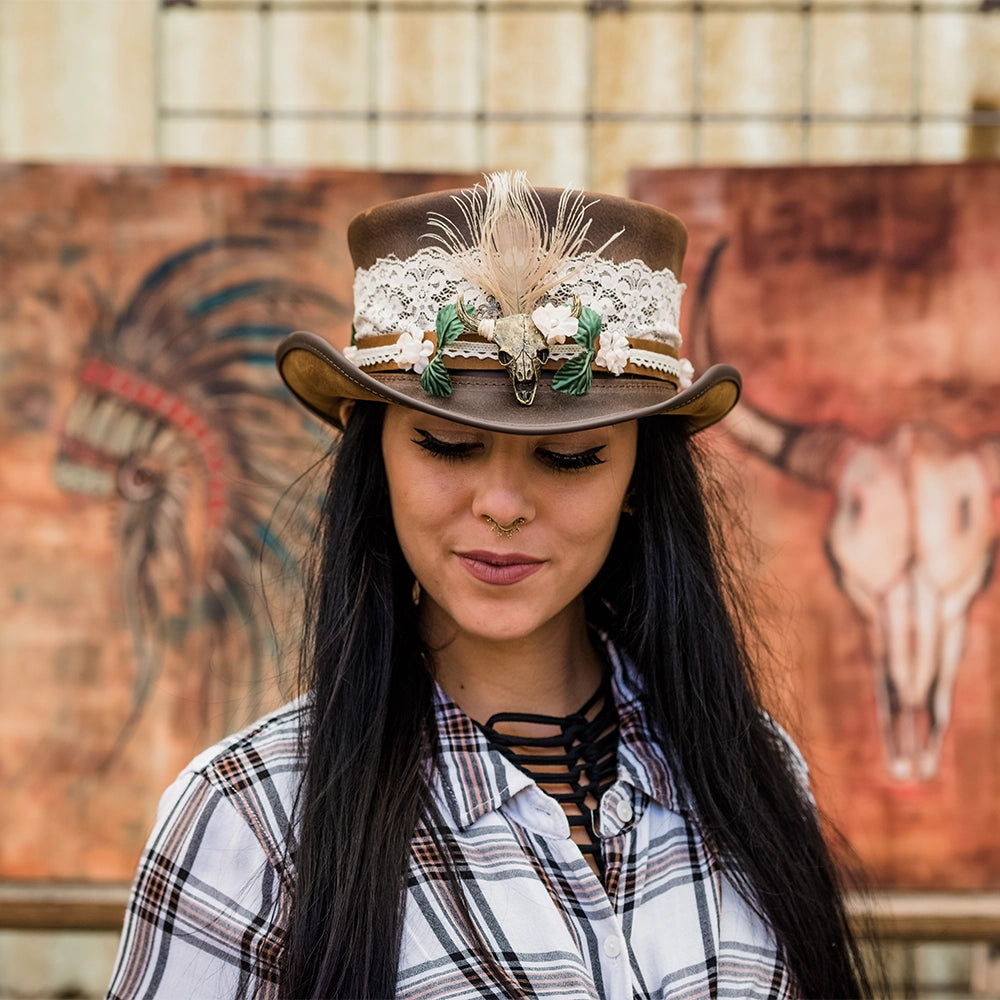 Woman wearing a decorative cowboy hat with a plaid shirt in front of a mural.