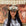 Woman wearing a decorative cowboy hat with a plaid shirt in front of a mural.
