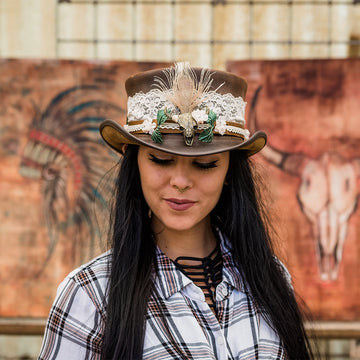 Woman wearing a decorative cowboy hat with a plaid shirt in front of a mural.