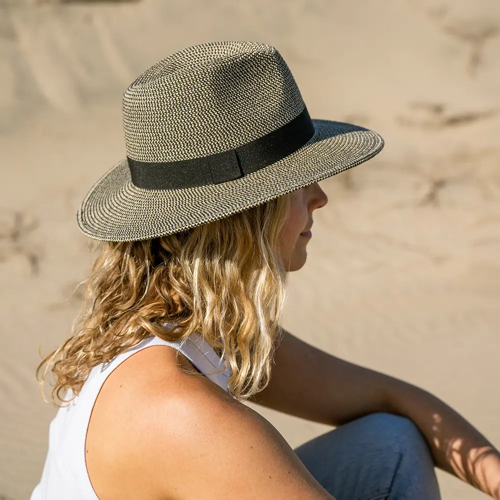 Person wearing a straw hat with a black band sitting on sand