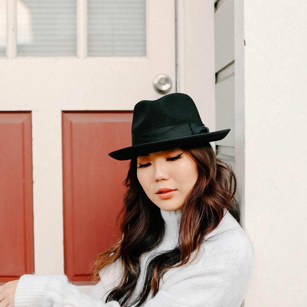 Woman wearing a black hat and white sweater in front of a door with red panels.