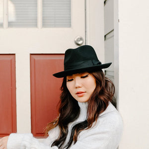 Woman wearing a black hat and white sweater in front of a door with red panels.