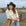 Woman wearing a black hat and light-colored shirt standing on a wooden dock by a body of water.