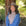 Woman wearing a beige hat and blue jacket standing next to a tree in a natural setting
