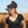Woman wearing a black cowboy hat with feathers in an outdoor setting