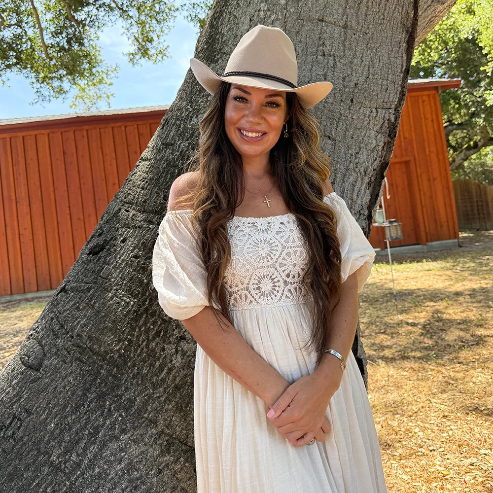 Woman in a white dress and hat standing next to a large tree