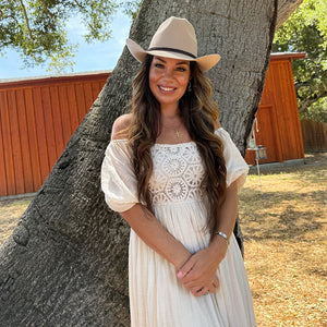Woman in a white dress and hat standing next to a large tree