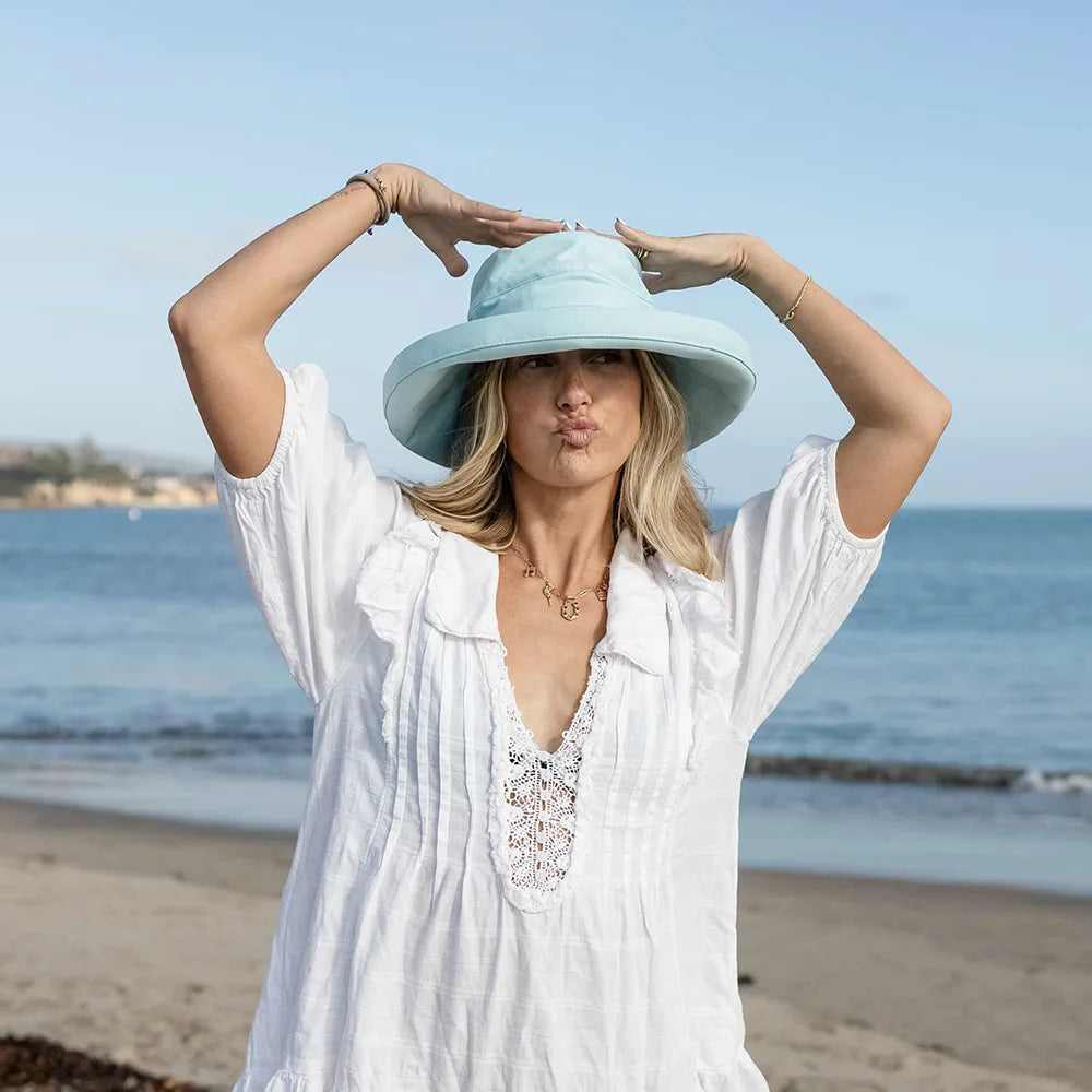 Woman wearing a light blue hat and white dress on a beach