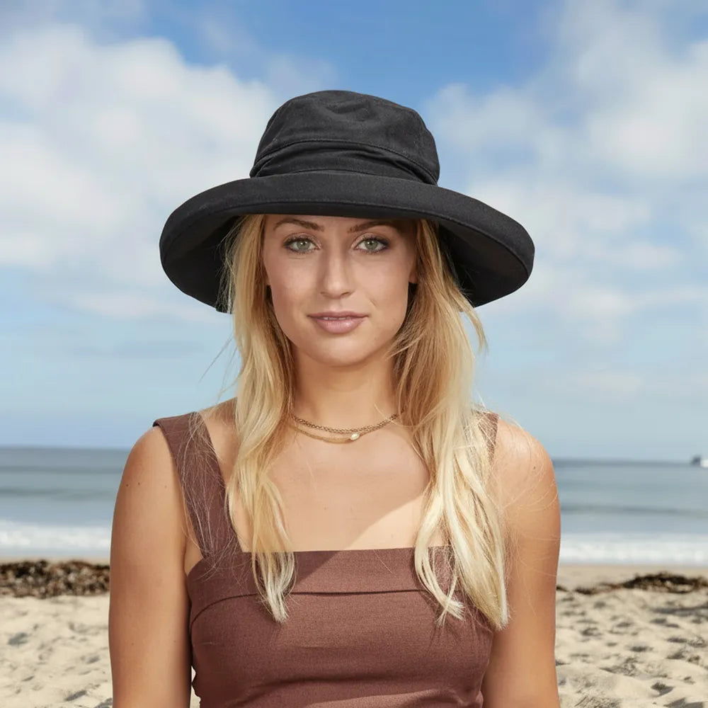 Woman wearing a black sun hat on a beach with a clear sky.