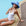 Woman in a white swimsuit and blue hat sitting by a pool.