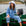 Woman sitting on a boat by the water, wearing a blue denim outfit and white sun hat.