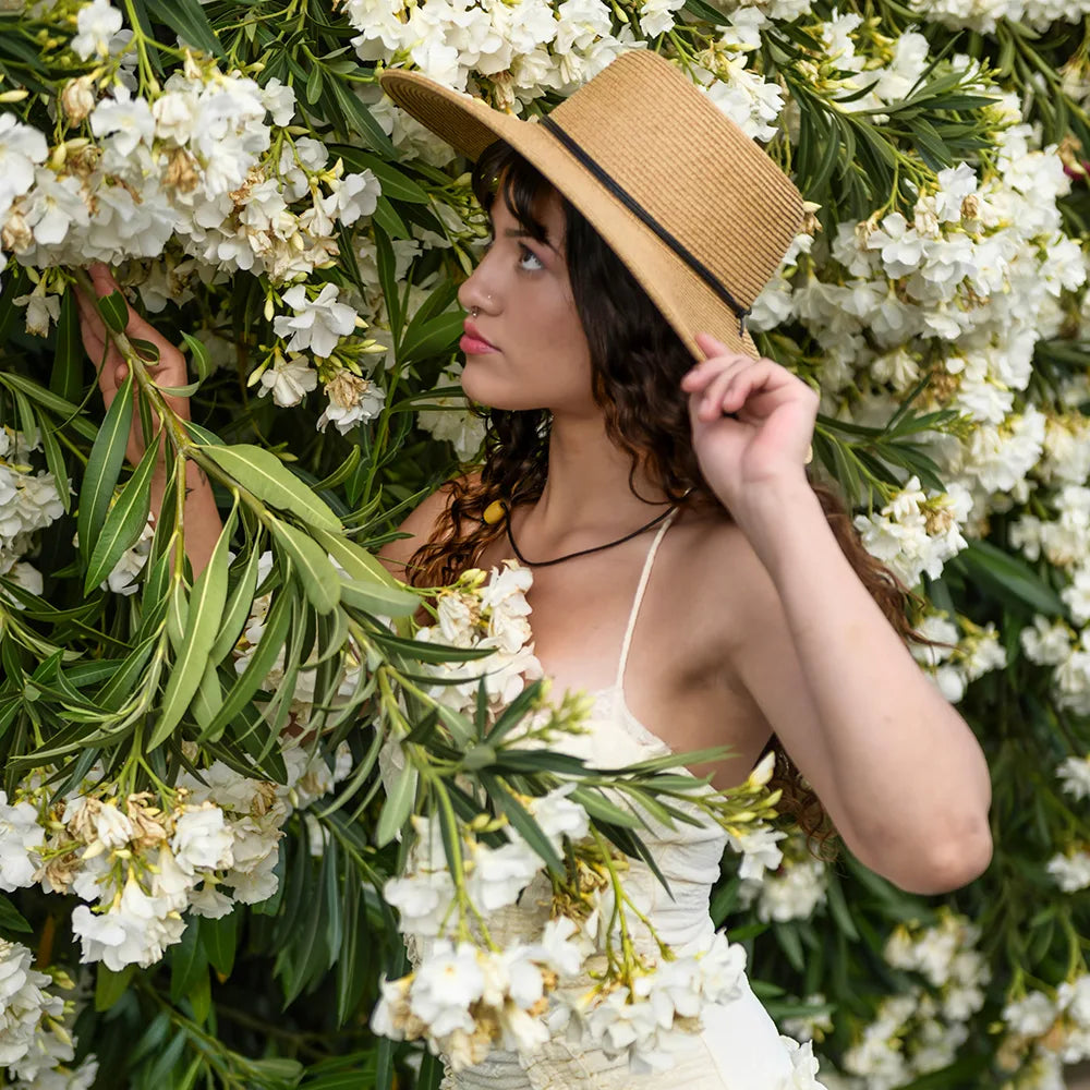 Woman wearing a straw hat and white dress among white flowers and green leaves