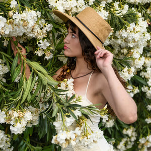 Woman wearing a straw hat and white dress among white flowers and green leaves