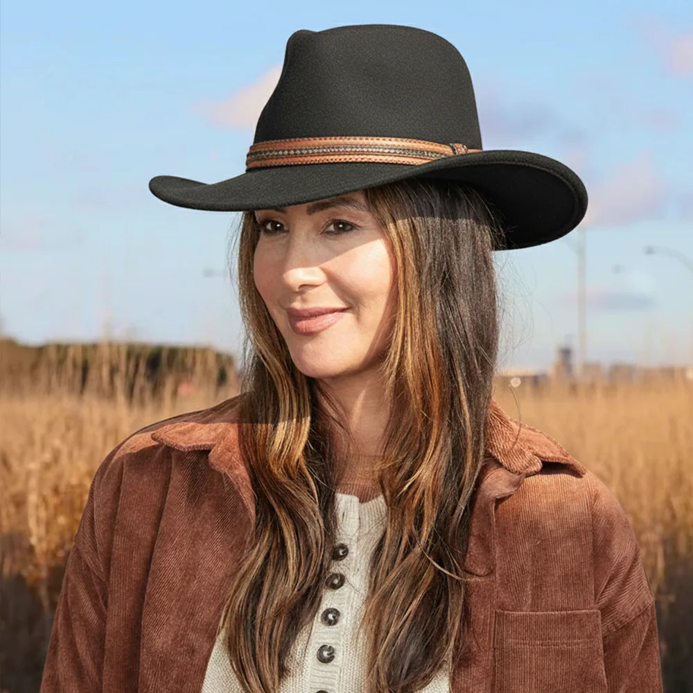 Woman wearing a black cowboy hat with a brown band, standing in a field.