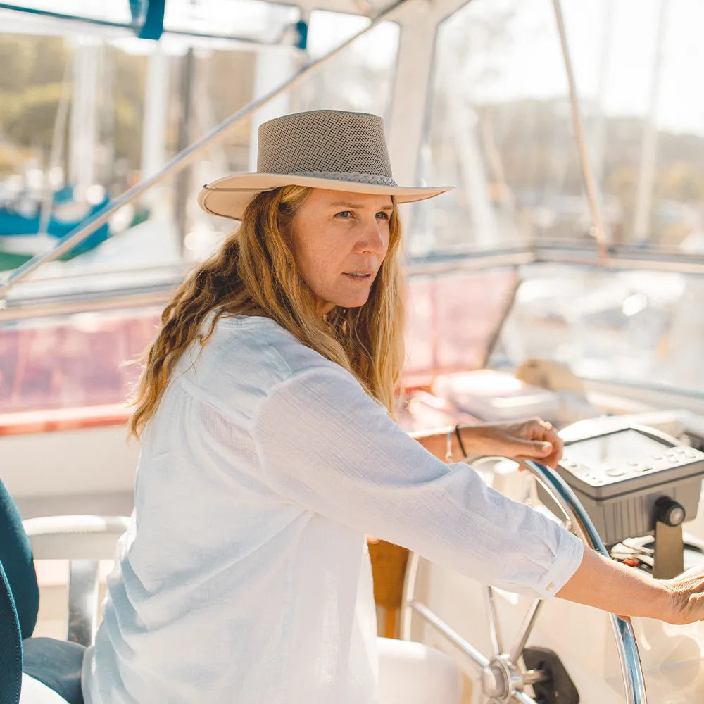Woman on a boat wearing a wide-brimmed hat and white shirt.