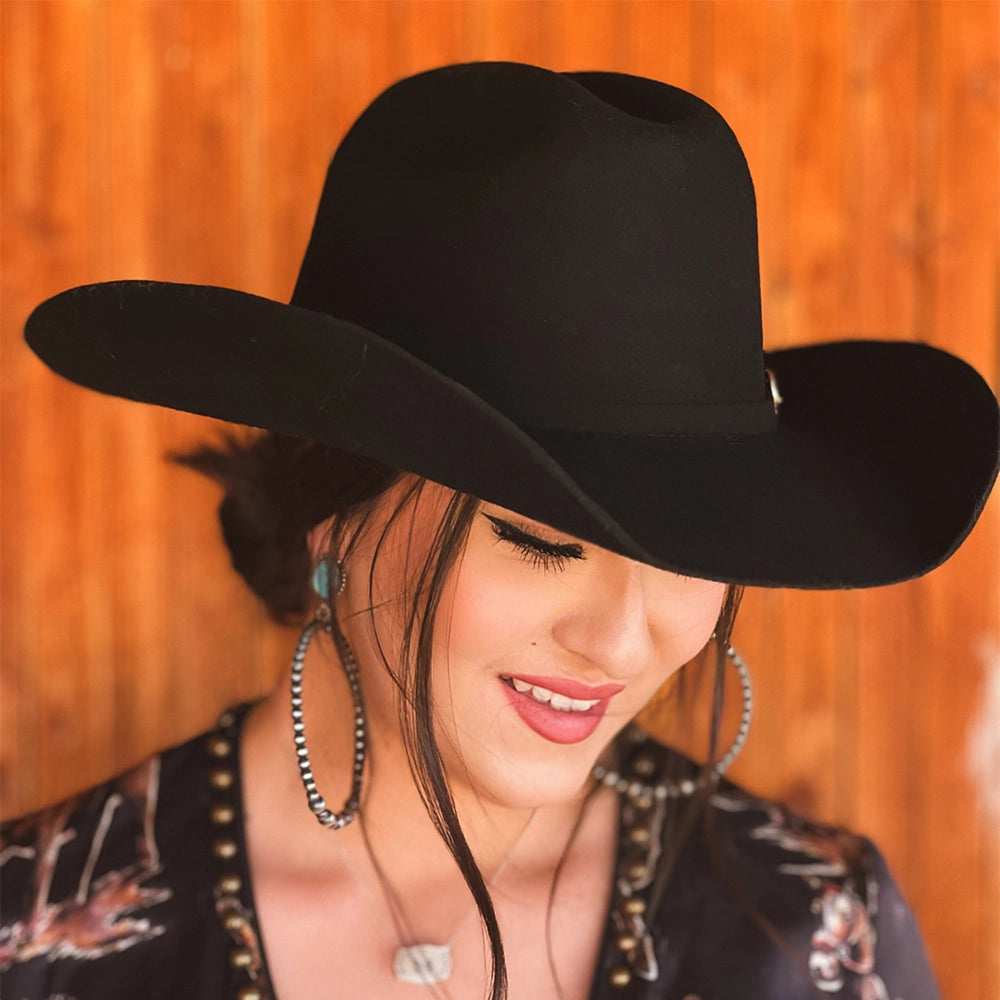 Woman wearing a black cowboy hat against an orange wooden background