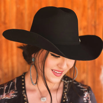 Woman wearing a black cowboy hat against an orange wooden background