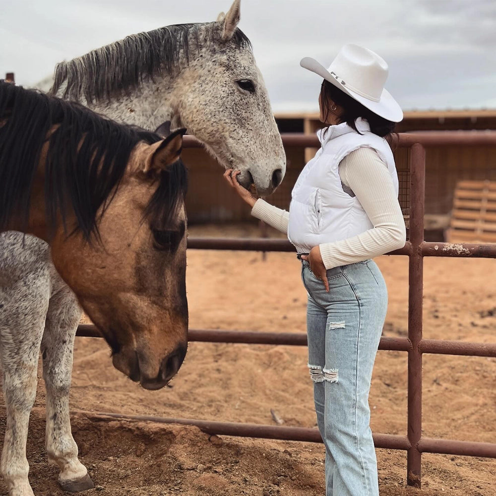 Woman in a cowboy hat petting a horse in a dirt arena.