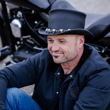 Man wearing a black hat and dark jacket sitting next to a motorcycle.
