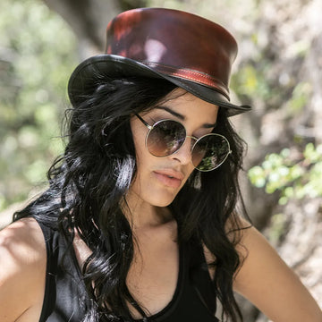 Woman wearing a brown leather hat and round sunglasses outdoors