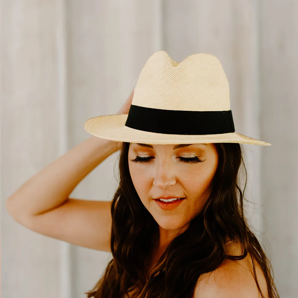 Woman wearing a straw hat with a black band against a neutral background