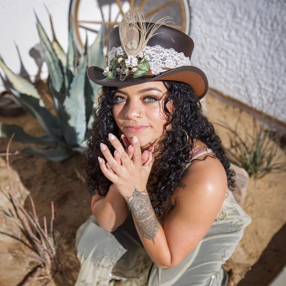 Woman wearing a decorative hat with lace and feathers in a desert-like setting
