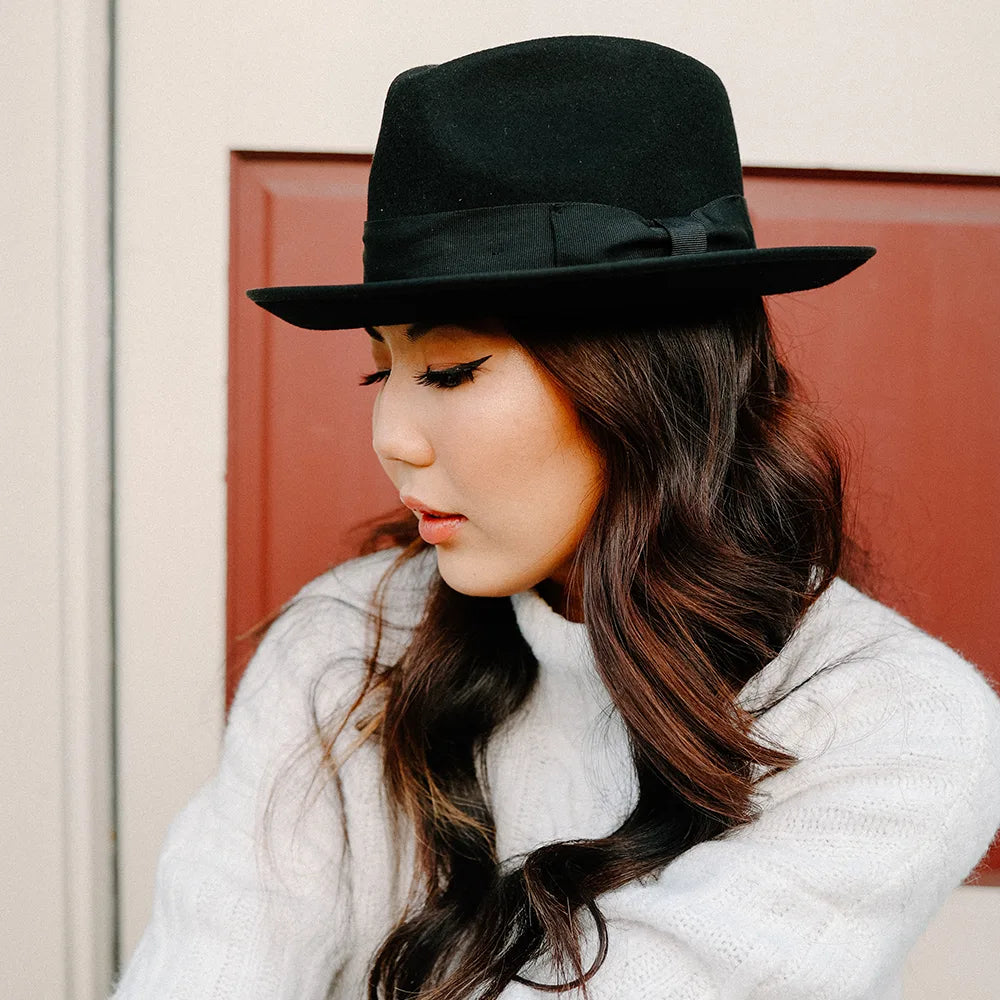 Woman wearing a black hat and white coat against a red door.
