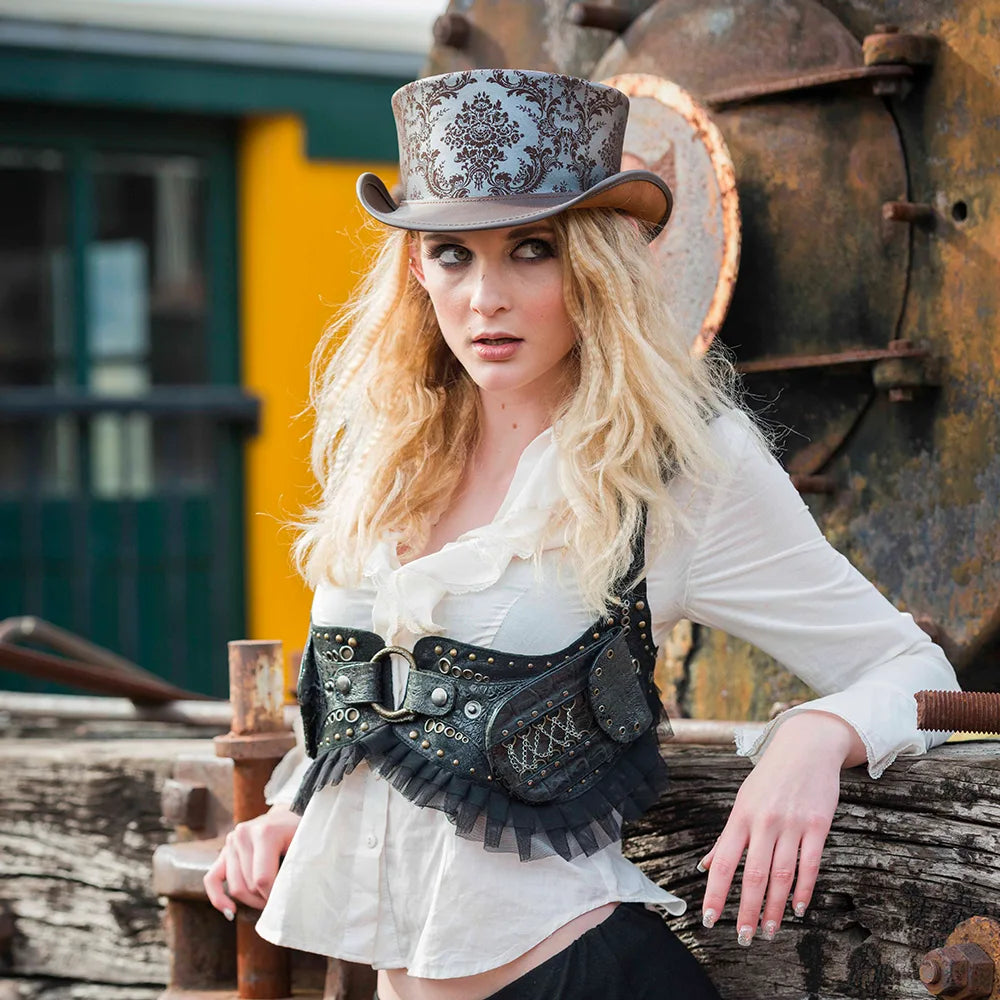 Woman in steampunk attire with a top hat and leather belt, leaning against a wooden structure.