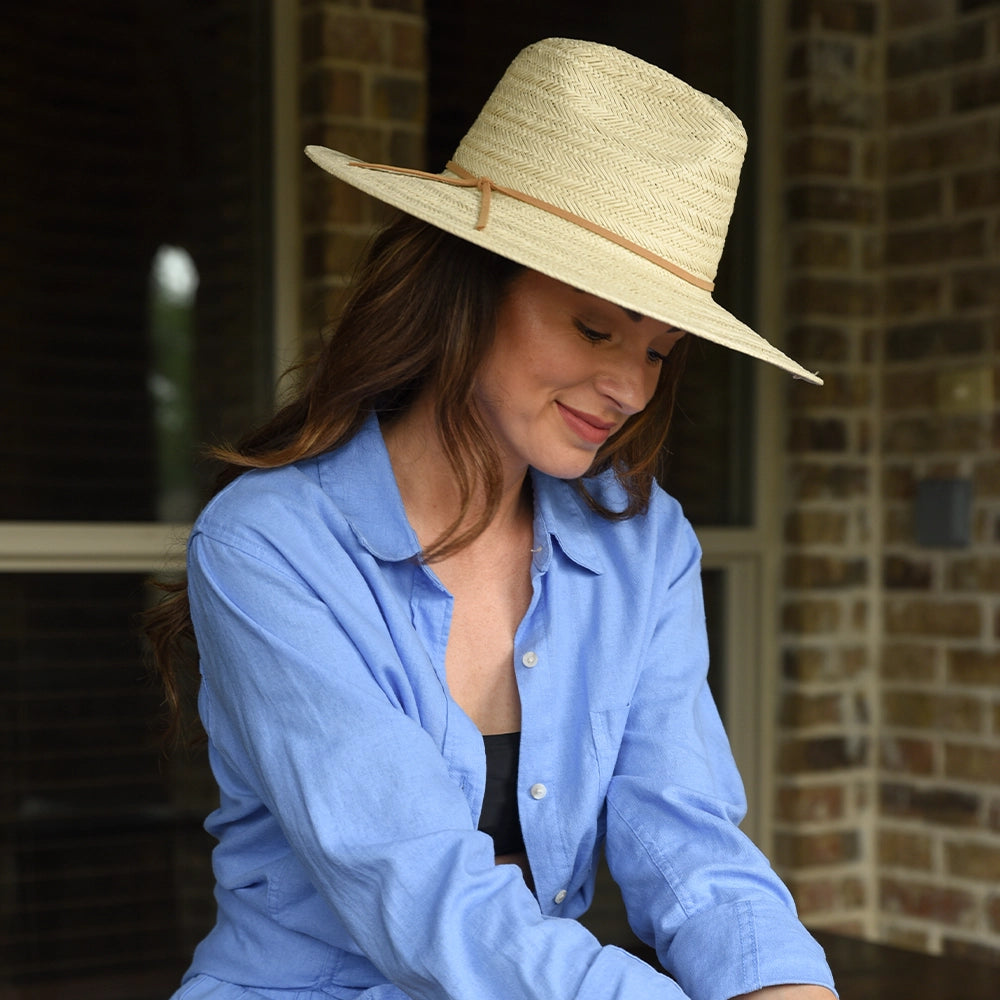 Woman wearing a straw hat and blue shirt sitting on a porch.