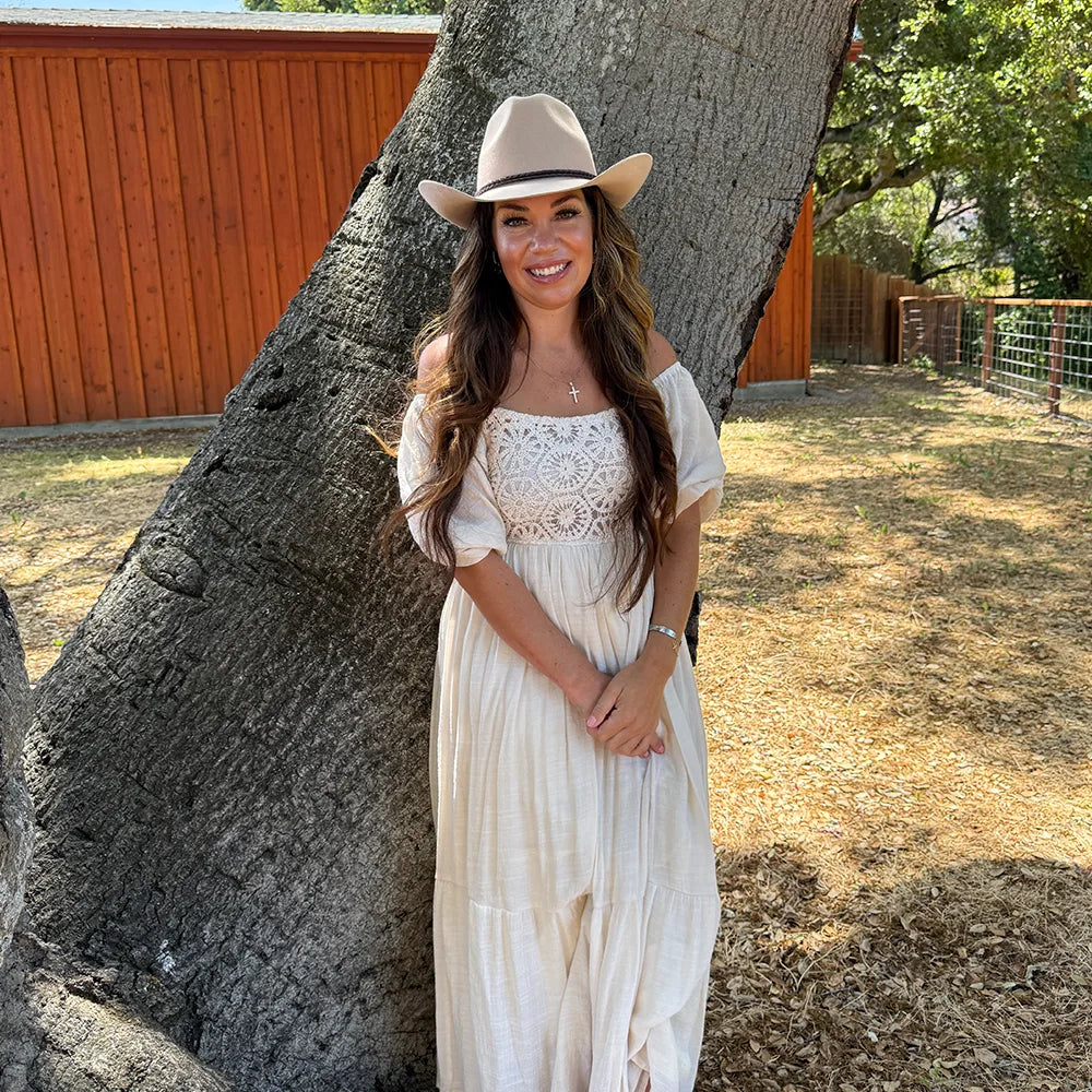 Woman in a white dress and hat standing next to a large tree