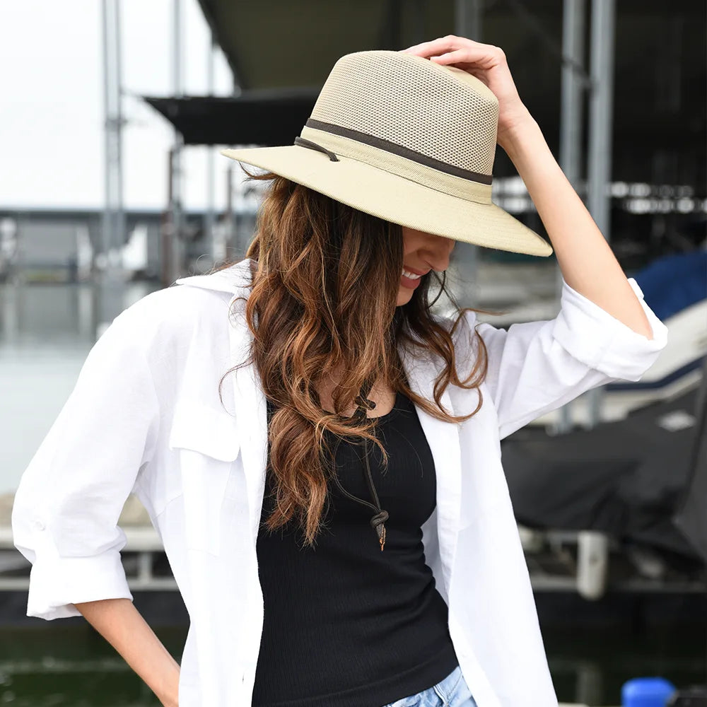 Woman wearing a beige hat with a black band, white shirt, and black top outdoors.