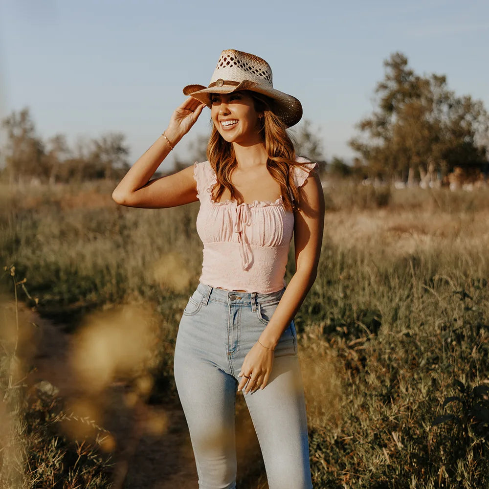 Woman wearing a pink top and denim shorts with a straw hat in a field.
