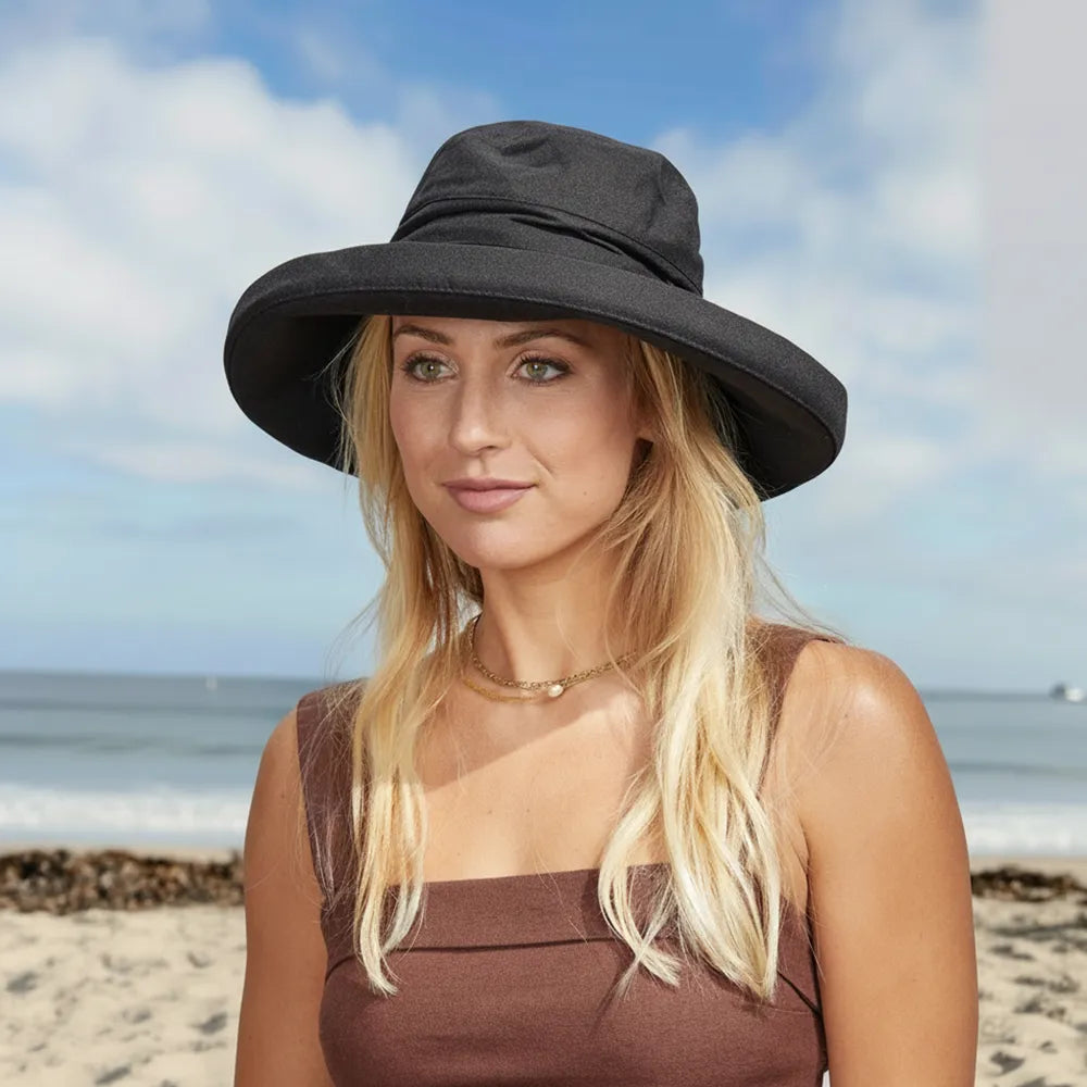 Woman wearing a black sun hat on a beach with ocean and sky in the background
