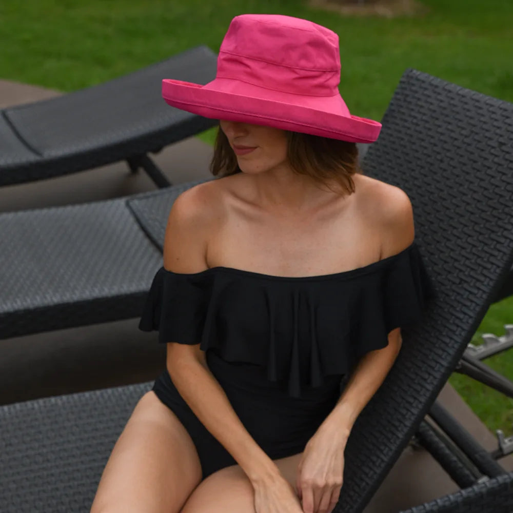 Woman wearing a black off-shoulder top and pink hat sitting on a lounge chair outdoors.