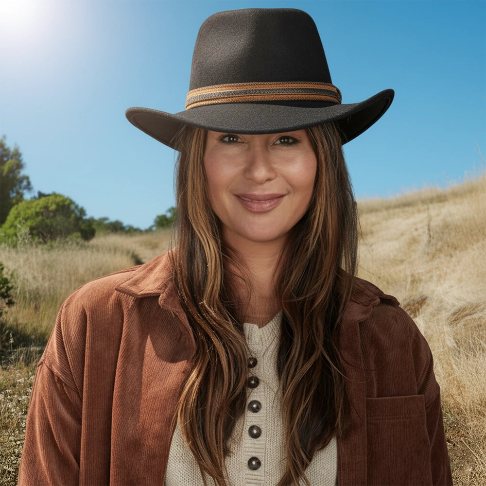 Woman wearing a brown hat and coat in an outdoor setting with trees and blue sky.
