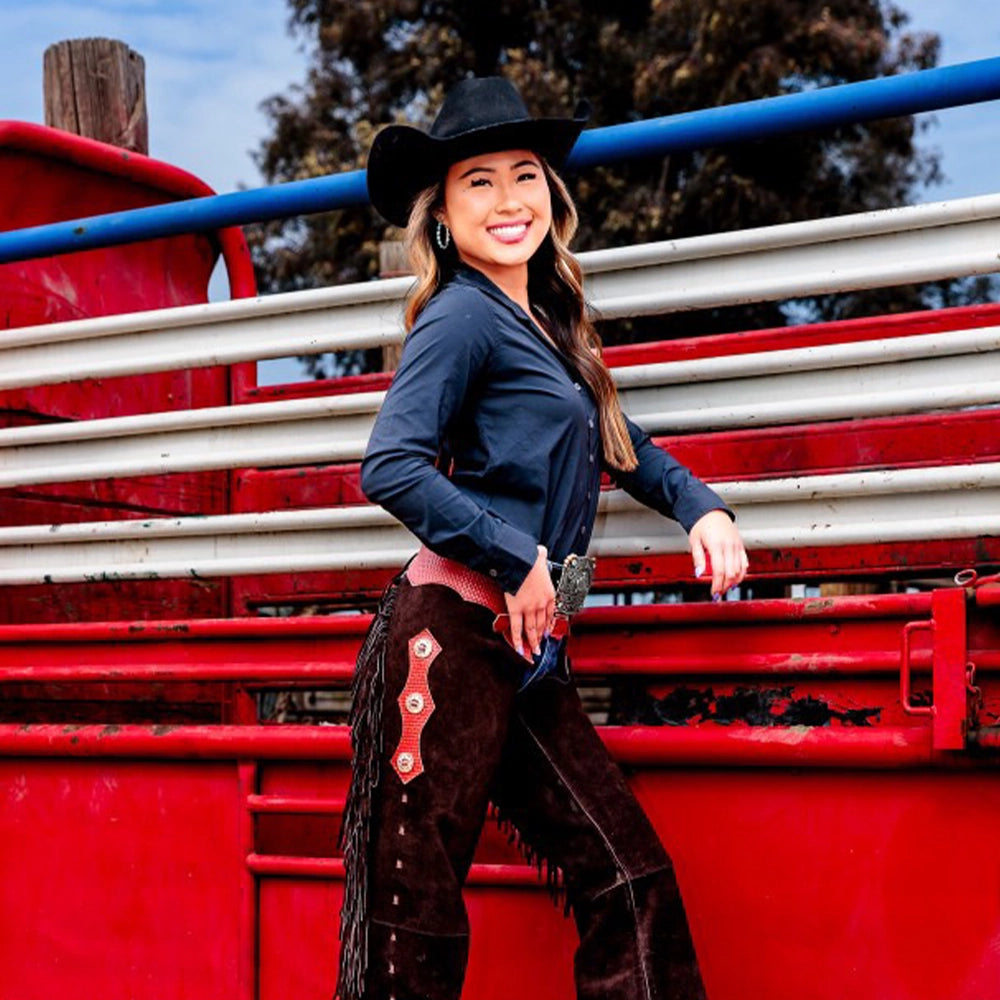 Woman in cowboy hat and outfit standing in front of a red and white livestock pen.