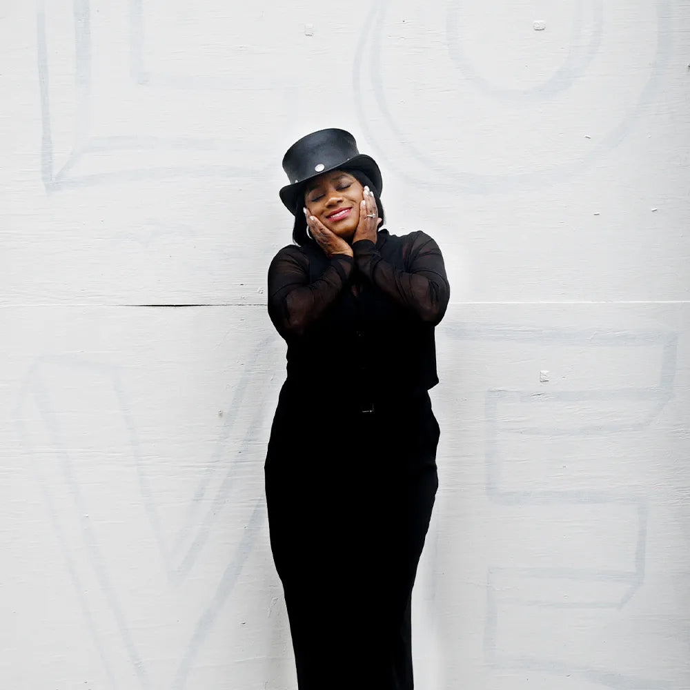 Person wearing a black outfit and hat against a white background