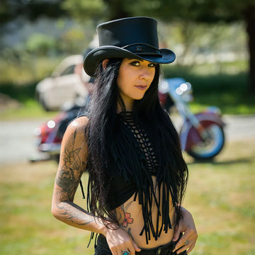 Person wearing a black top hat and fringe scarf in an outdoor setting with blurred background