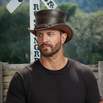 Man wearing a brown leather hat in front of a railroad crossing sign with trees in the background