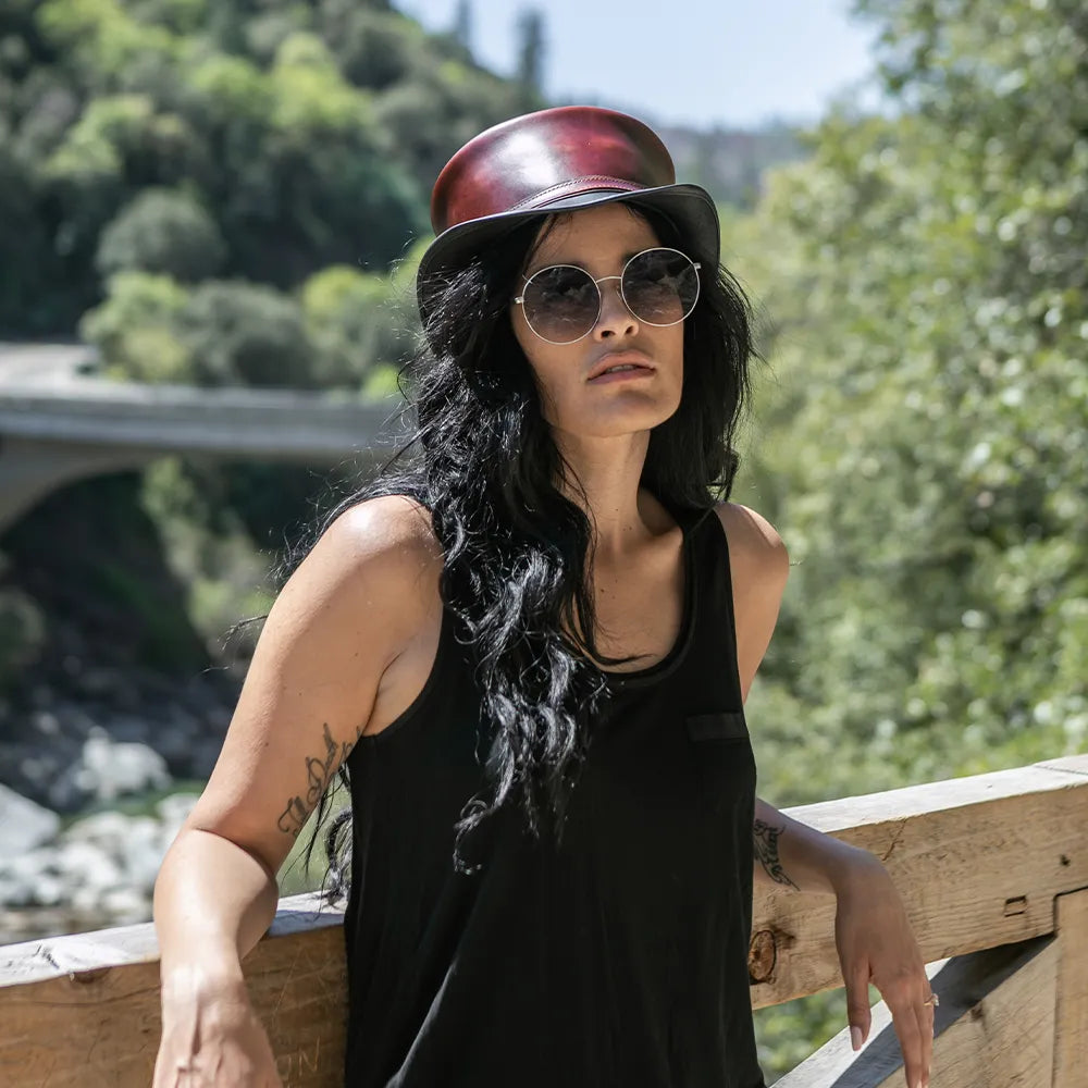 Person wearing a black tank top and sunglasses, standing outdoors with greenery in the background