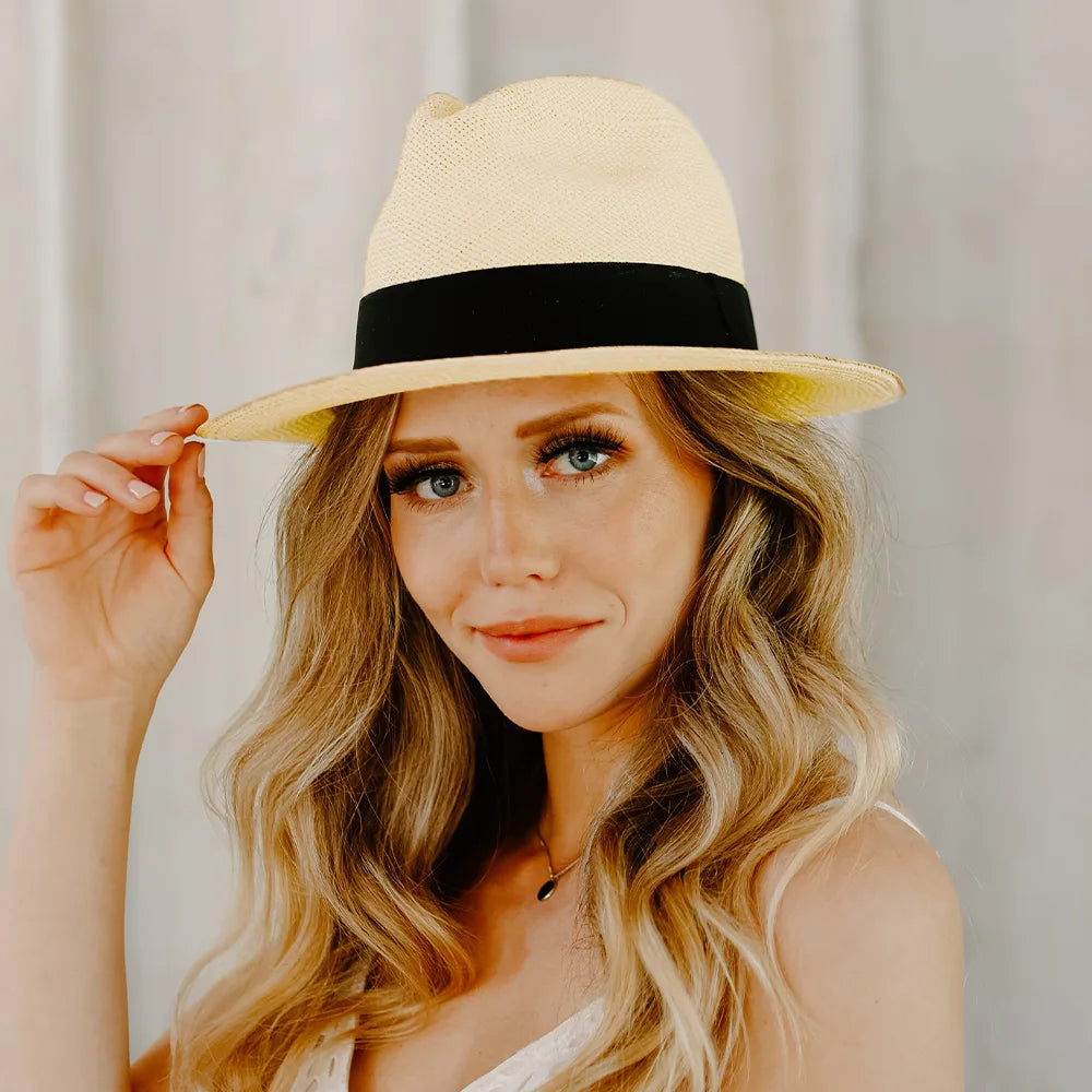 Woman wearing a beige hat with a black band against a neutral background